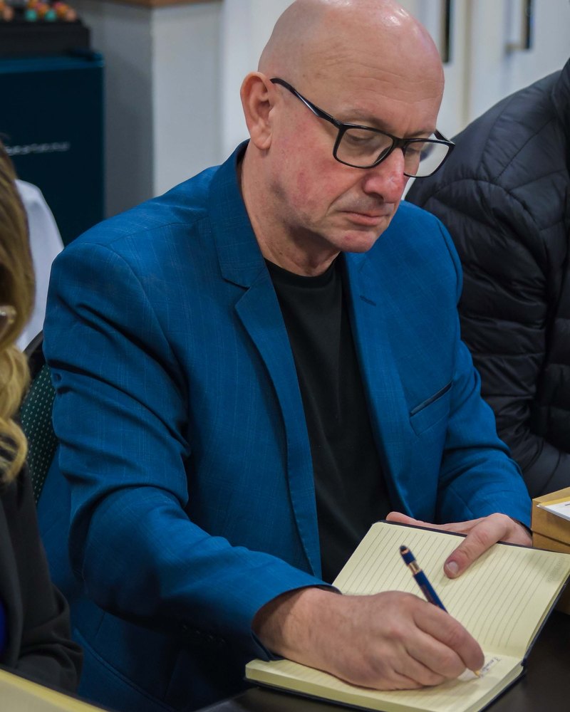 Edmilson Rene Bachmann de blazer azul, anotando em um caderno durante uma reunião